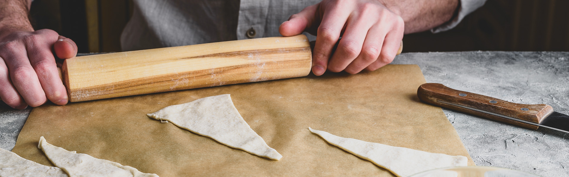 Bäcker formt Croissant-Teig mit Wahlholz auf Backfolie