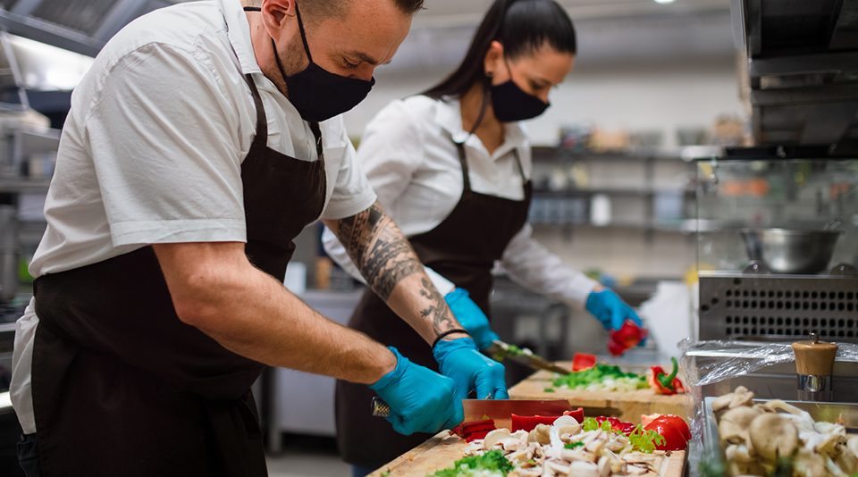 Zwei Personen in Schutzbekleidung schneiden in einer Restaurantküche Gemüse