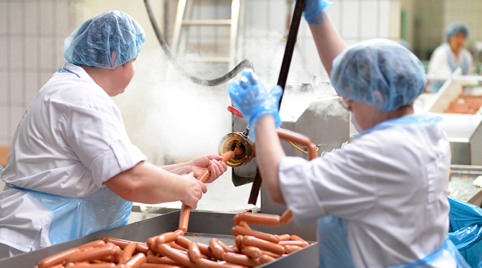 Zwei Personen mit Schutzbekleidung stellen in einer Fleischerei Wurstwaren her