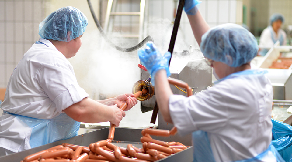 Zwei Personen mit Schutzbekleidung stellen in einer Fleischerei Wurstwaren her