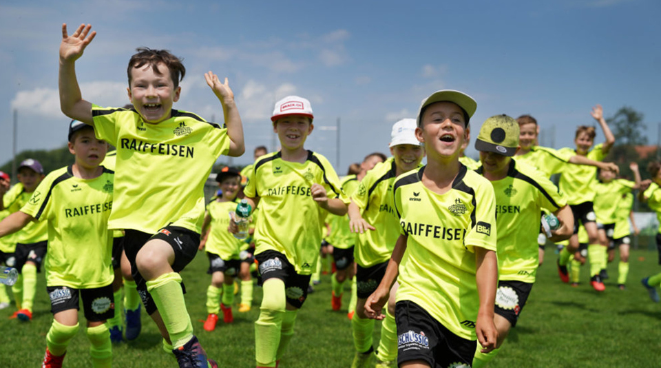 Kinder in Trikots rennen über Fussballfeld