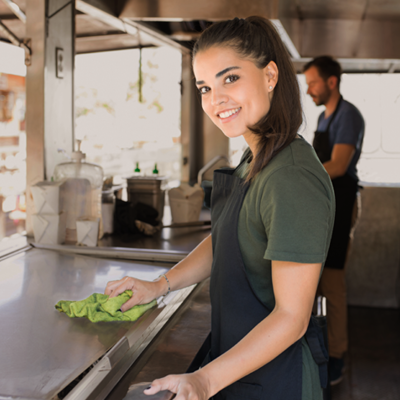 Frau in Food-Truck reinigt Theke mit Putzlappen