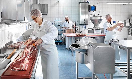 Mitarbeiter in Schutzbekleidung von Pacovis verarbeiten Fleischwaren in der Lebensmittelproduktionsstätte