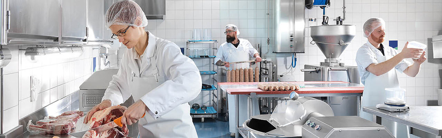 Drei Personen verarbeiten Fleisch in der Lebensmittelproduktion in Schutzbekleidungen der Pacovis