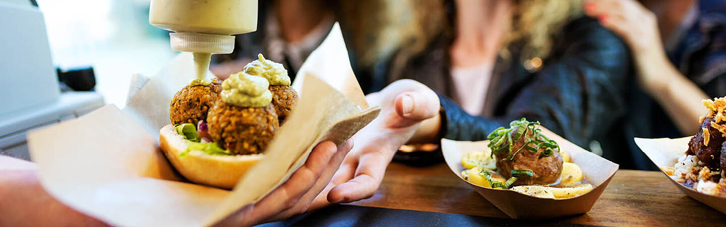 Person würzt Take-away-Essen mit Sauce und überreicht das Essen dem Kunden